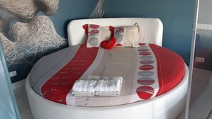 A bed with a red and white striped bedspread, two pillows, a red heart-shaped pillow, and a folded white towel.
