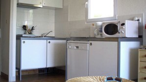 Een kleine keuken met witte kastjes, een magnetron en een vaatwasser.
