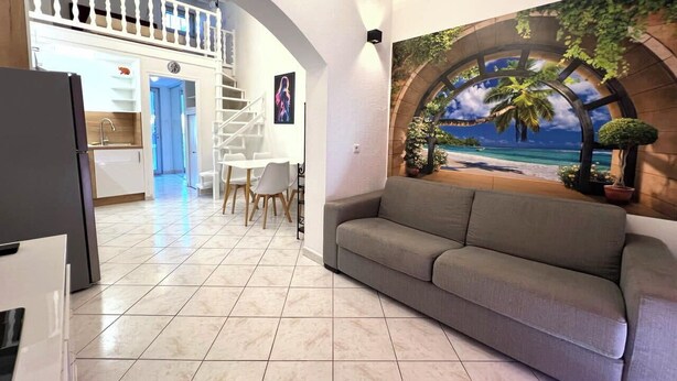 Ein Wohnzimmer mit einer Couch, ein Essbereich mit Stühlen, eine Küche mit Schränken und eine Treppe, die zu einer oberen Ebene führt.