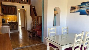 Ein Essbereich mit einem Glastisch und Holzstühlen, eine Treppe, die in einen anderen Raum führt, und eine Küche im Hintergrund.