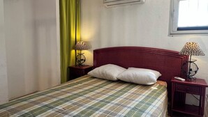 Ein Schlafzimmer mit kariertem Überwurf, einem roten Kopfteil, zwei Nachttischen mit Lampen, einem Fenster mit Blick und einer Wandklimatechnik.