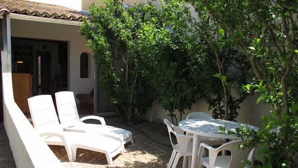 Eine Terrasse mit weißen Plastikstühlen und einem Tisch, umgeben von Pflanzen und einem Fliesenboden.