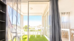 Una habitación con puerta corrediza de vidrio que da a un balcón con césped verde y sillas blancas.