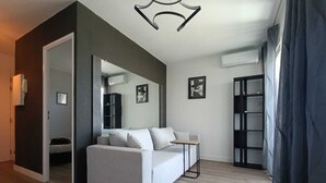 Una sala de estar moderna con un sofá blanco, una mesita auxiliar y un espejo. Se ve una estantería y un cuadro enmarcado en la pared.
