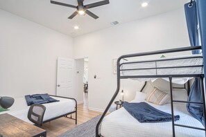 A dormitory room with two bunk beds, a desk, a chair, and a ceiling fan.