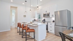 A modern kitchen with white cabinetry, a central island with bar stools, stainless steel appliances, and pendant lighting. - Feel Chill and Enjoy 4BR 3BA Near Fun Riverwalk (San Antonio)