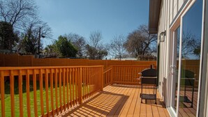 A wooden deck with a grill and a chair, surrounded by a wooden fence and a glass door leading to a covered patio area. - Feel Chill and Enjoy 4BR 3BA Near Fun Riverwalk (San Antonio)