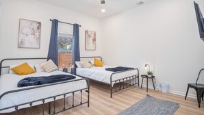 Un dormitorio moderno con dos camas, un ventilador de techo y una mesita de noche con lámpara.