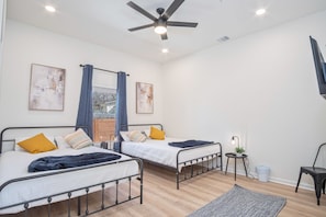 Un dormitorio moderno con dos camas, un ventilador de techo y una mesita de noche con lámpara.