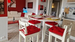 A dining area with a round table, white chairs with red cushions, and a red sofa in the background. - Naturiste Cap d'Agde Héliopolis F 61 (Agde)