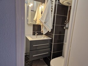 Een badkamer met een witte wastafel, donkere betegelde wanden en een wit toilet.