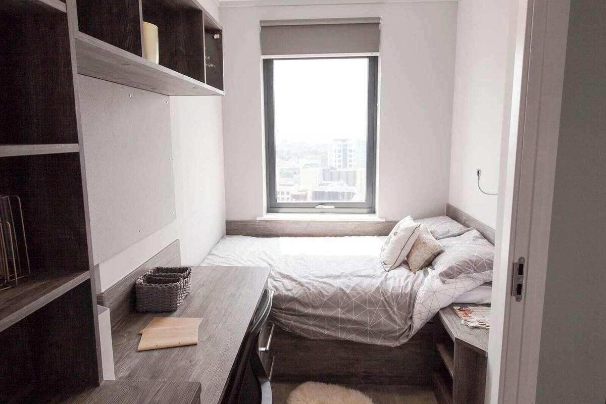 A compact bedroom with a bed, a desk, and a large window.