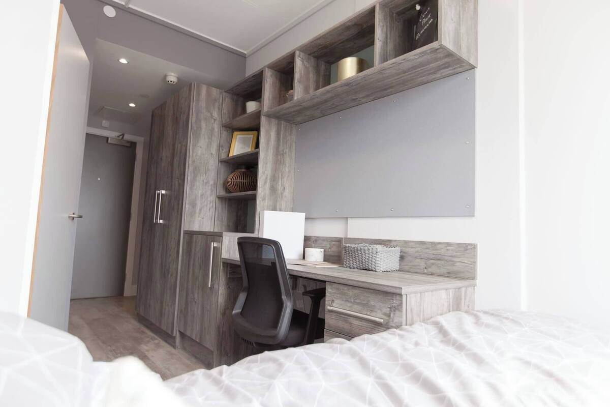 A bedroom with a bed, a desk with a chair, and a wardrobe.