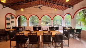 An indoor dining area with wooden tables and chairs, arched windows, and a ceiling fan.