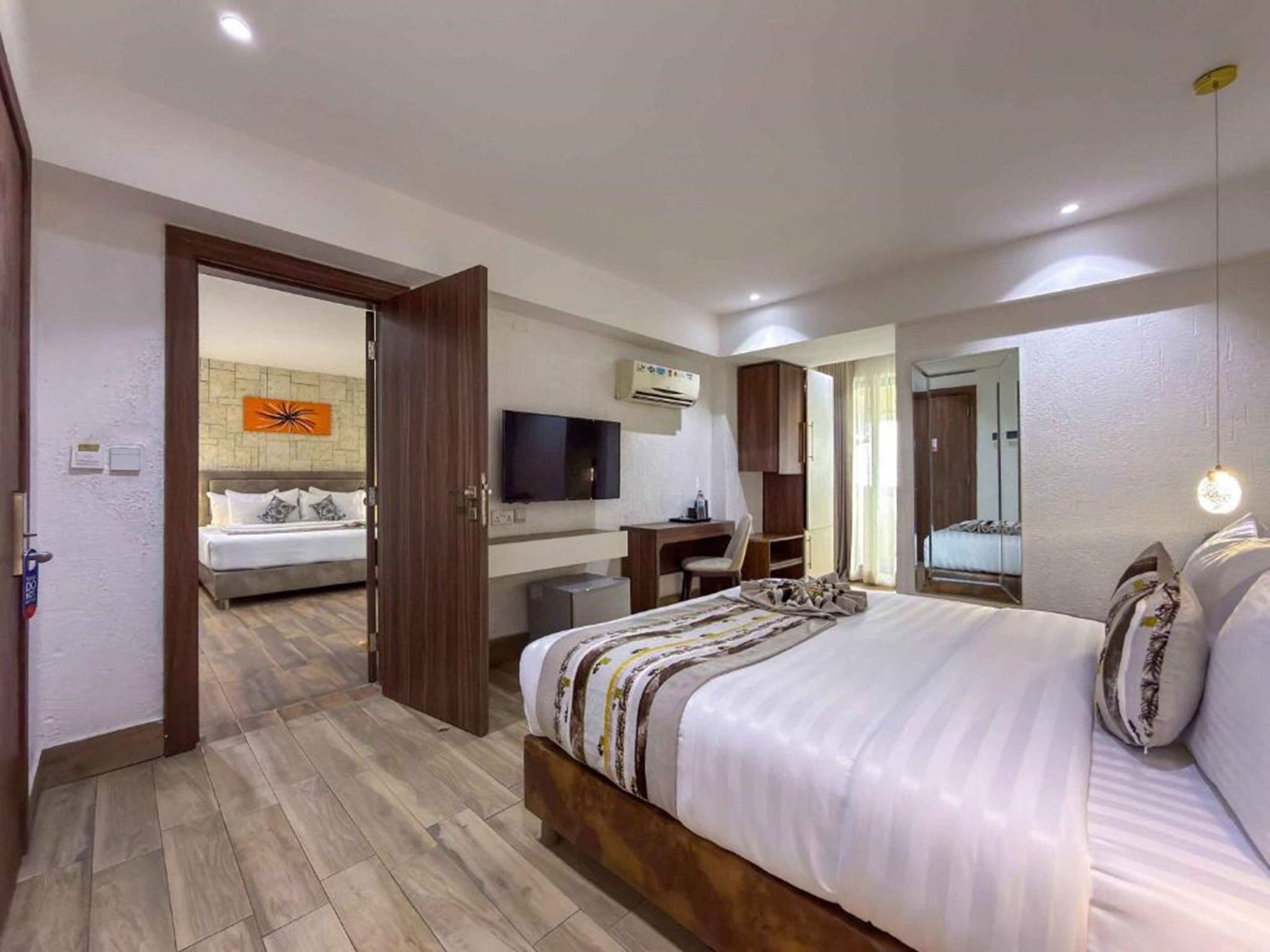 A hotel room with a large bed, a desk, a television, and a mirror.