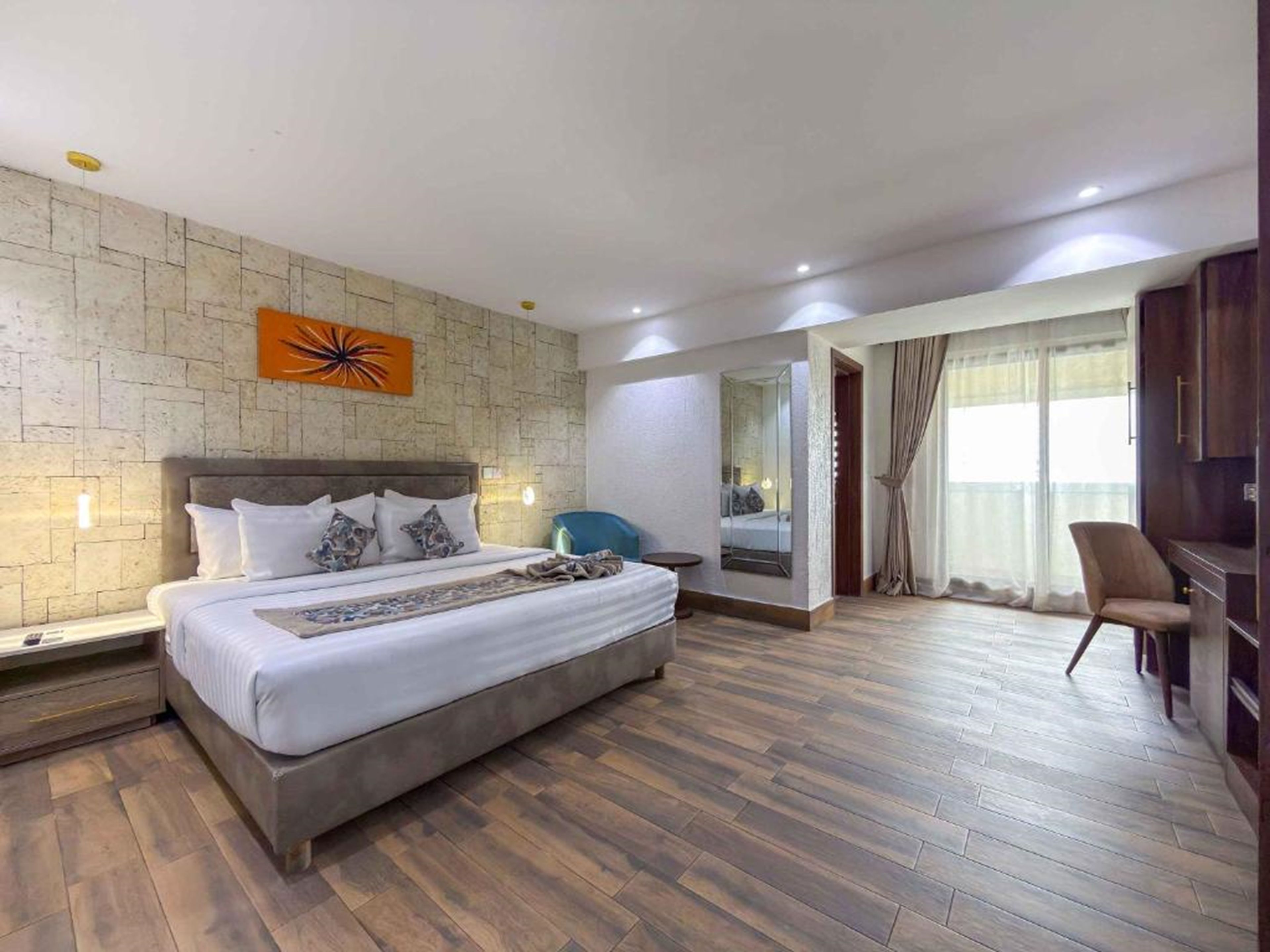 A modern hotel room with a large bed, a mirror, a seating area, and a view of the outdoors.