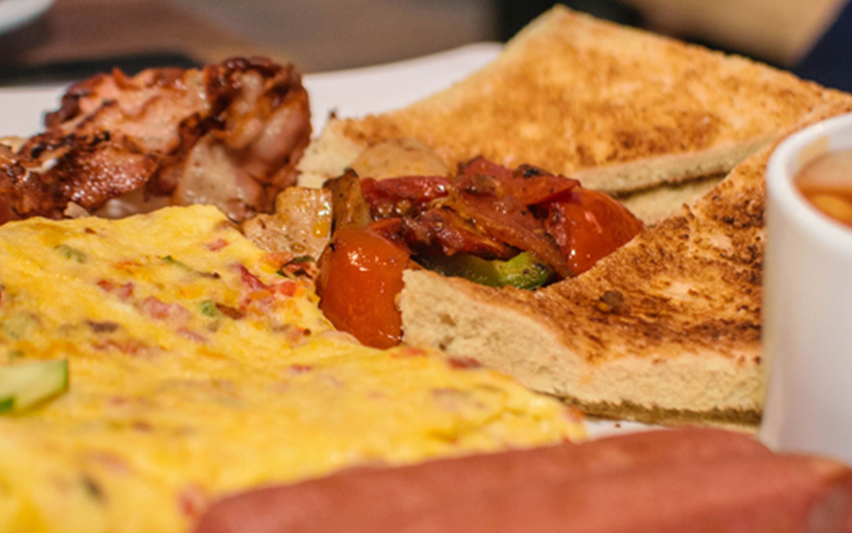 A breakfast plate with toast, bacon, eggs, and tomatoes.