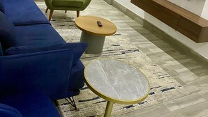Ein modernes Wohnzimmer mit einem Ecksofa, einem grünen Sessel, einem runden Couchtisch, einem kleinen Beistelltisch, einem flachbildfernseher an der Wand und einer Holztruhe für Unterhaltungselektronik.