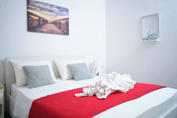A neatly made bed with a red blanket, white pillows, and a white headboard.