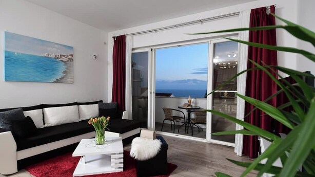 A modern living room with a black and white sofa, a red rug, and a painting of a coastal scene. - Charming 2-bedroom apartment with WiFi, AC in enchanting Dubrovnik (Dubrovnik)