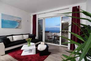 A modern living room with a black and white sofa, a red rug, and a painting of a coastal scene.