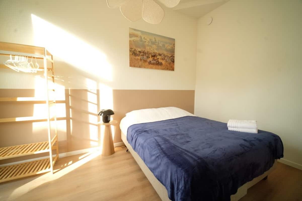 A bedroom with a bunk bed, a single bed, a painting of a safari scene, and a bedside table with a lamp.