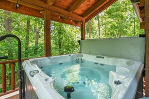 Een hottub op een houten terras, met uitzicht op een bos.