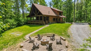 A log cabin with a porch, surrounded by a gravel path and a fire pit area with chairs. - Falling Leaves | Hocking Hills, Accessible, Pets (South Bloomingville)