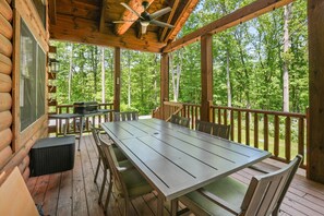 A wooden deck with a table and chairs, surrounded by a wooden railing, overlooking a forest.