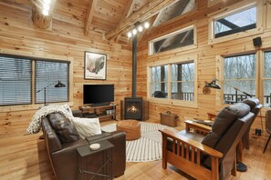 A cozy log cabin interior with a fireplace, leather furniture, and large windows.
