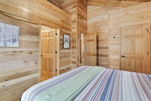 A wooden cabin room with a bed, wooden walls, and doors.