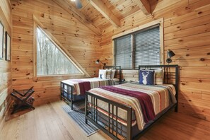 Een slaapkamer in een houten hutje, met twee bedden, een groot raam en uitzicht op bomen.