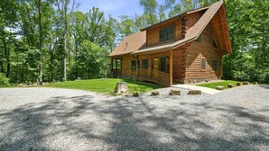 A log cabin with a porch, surrounded by a gravel driveway and a forested area. - Falling Leaves | Hocking Hills, Accessible, Pets (South Bloomingville)
