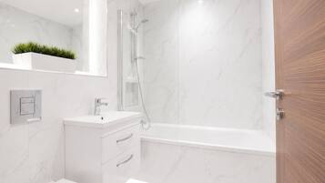 A modern bathroom with a white marble wall, a built-in sink, a toilet, and a shower enclosure.