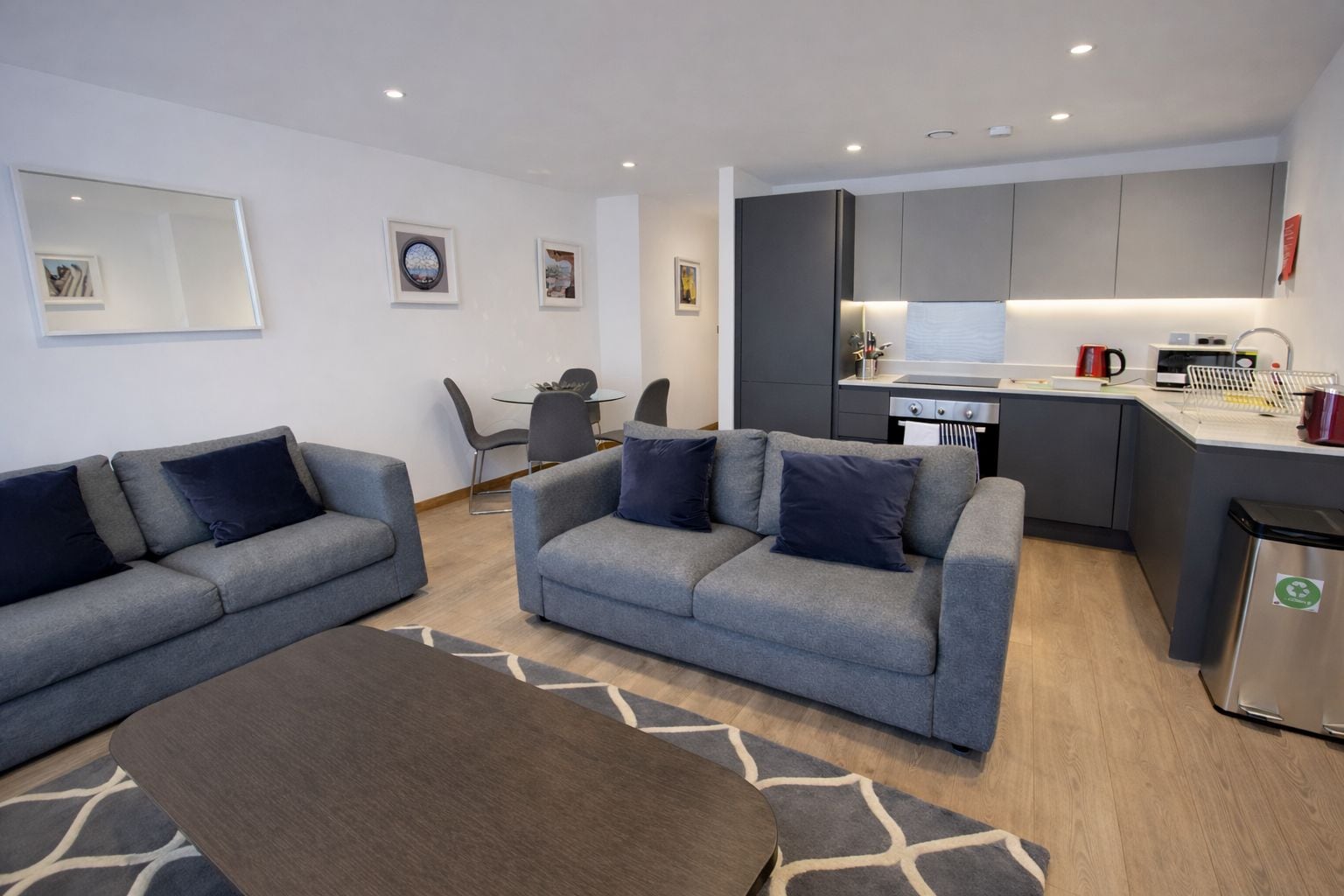 Un salon moderne avec des canapés gris, une table basse et un coin repas avec des chaises.