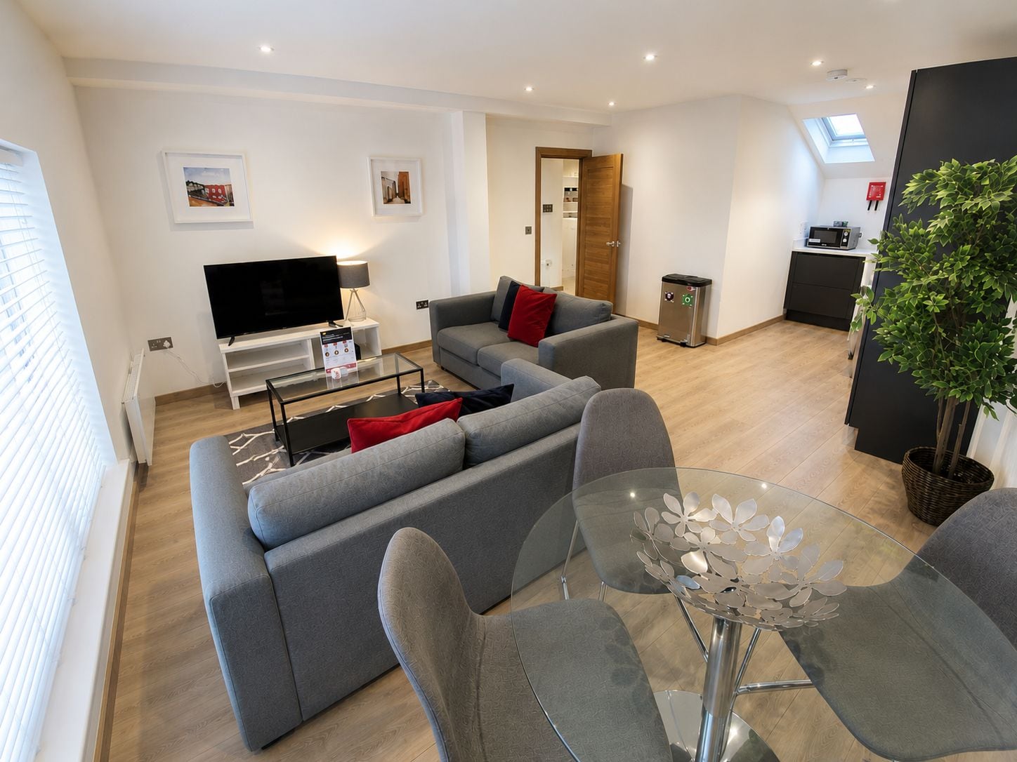 A modern living room with a grey sofa, a glass coffee table, and a TV.