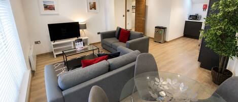 A modern living room with a grey sofa, a glass coffee table, and a TV.