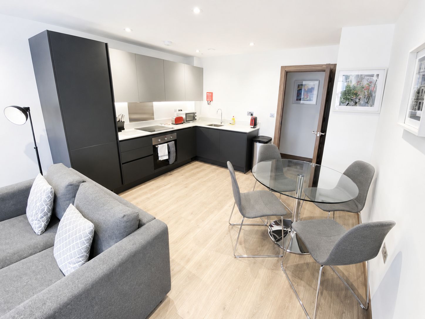 A modern kitchen with a dining area, a sofa, and a glass table.