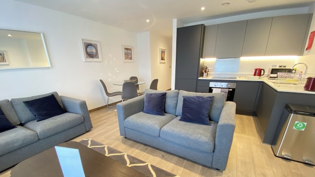 Una sala de estar moderna con dos sofás grises, una mesa de centro y un comedor con sillas y una mesa.