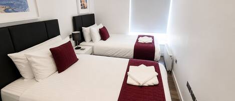 A hotel room with two beds, a nightstand, a lamp, and a window with blinds.
