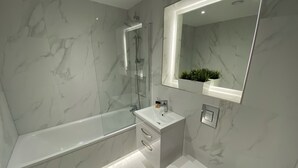 Un baño moderno con una bañera de hidromasaje con mampara de vidrio, un lavamanos blanco y un inodoro.