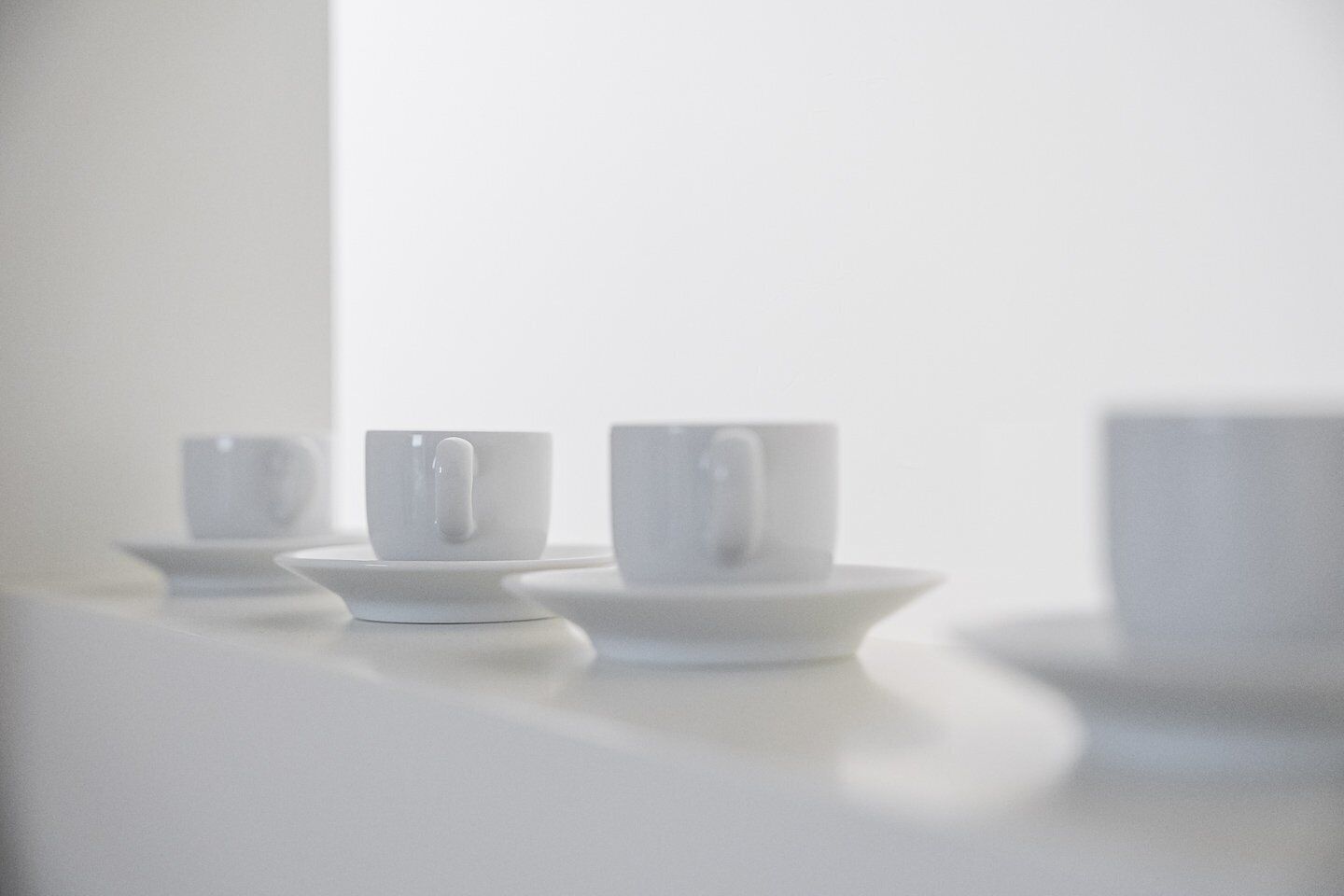 Three white cups on saucers on a white surface.