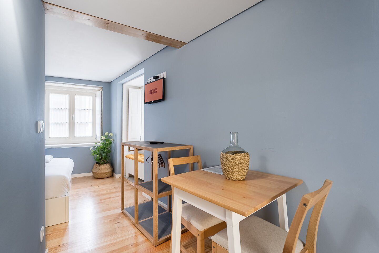A compact room with a wooden table, chairs, a small potted plant, and a wall-mounted TV.