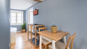 A compact room with a wooden table, chairs, a small potted plant, and a wall-mounted TV. - GuestReady - Souto Downtown Studio 1 (Porto)