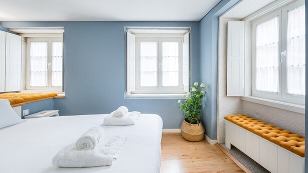 A modern hotel room with a large bed, two windows, a potted plant, and a bench by the window. - GuestReady - Souto Downtown Studio 1 (Porto)