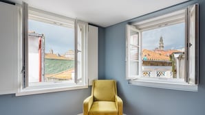 A room with two open windows, a yellow chair, and a view of buildings and a tower. - GuestReady - Souto Downtown Studio 3 (Porto)