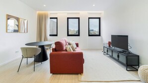 Ein modernes Wohnzimmer mit einem roten Sofa, einem runden Esstisch und einem Fernseher auf einer Kommode.
