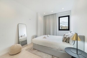 Une chambre d’hôtel moderne avec un grand lit, une table de chevet, une lampe, un miroir et une vue sur la ville par la fenêtre.