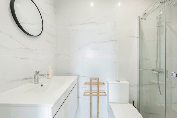 Une salle de bain moderne avec un mur en marbre blanc, une cabine de douche en verre et un porte-serviettes en bois.