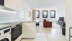 Eine moderne Küche mit Einbauofen und Mikrowelle, ein Essbereich mit Tisch und Stühlen, ein rotes Sofa und ein Fernseher in einer Ecke.